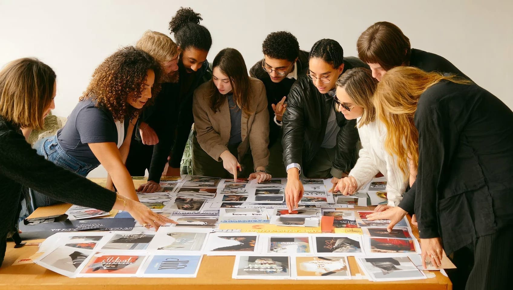 A JULY creative team gathered around a worktable, reviewing campaign layouts and comps spread across the surface